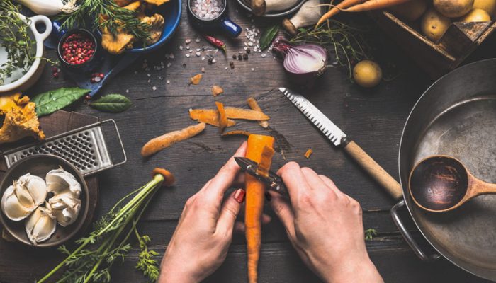 Person Peeling Carrots At A Table Covered With Food And Cookware