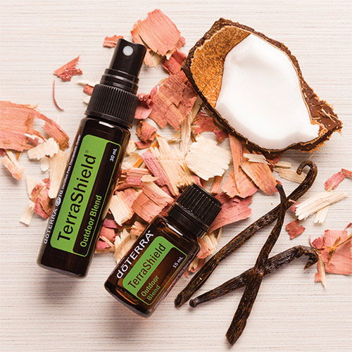 TerraShield oil bottle and spray bottle laying over cedarchips, vanilla beans, and fresh coconut